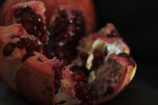 La grenade ouverte repose sur un fond noir. grains rouges brillent. macro photographie dark-key . — Photo