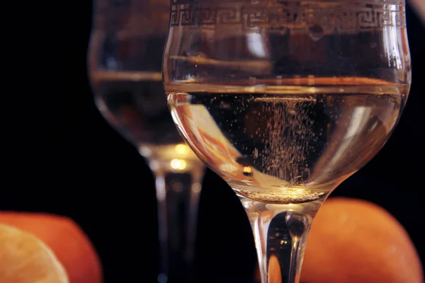 Duas taças de champanhe em um fundo preto com tangerinas. Bolhas de vinho espumante em um copo . — Fotografia de Stock