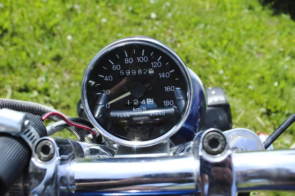 Speedometer on a motorcycle on the steering wheel, which stands on the green lawn — Stock Photo, Image