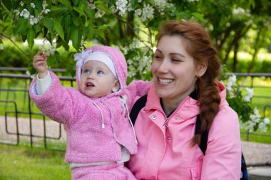 Annem çiçek açan bir elma ağacının gölgesinde çimlerin üzerinde oturur. Oynuyor ve kızlarına sarılıyor..