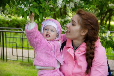 Annem çiçek açan bir elma ağacının gölgesinde çimlerin üzerinde oturur. Oynuyor ve kızlarına sarılıyor..