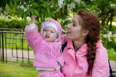 Annem çiçek açan bir elma ağacının gölgesinde çimlerin üzerinde oturur. Oynuyor ve kızlarına sarılıyor..