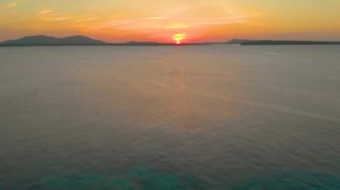 4k Havadan deniz üzerinde turuncu gün batımı görüntüsü ve Onok Adası, Balabac, Filipinler 'deki Palawan' da okyanus yüzeyine yansıyan güneşi yansıtıyor.
