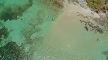 Timbayan Adası 'ndaki turkuaz gök mavisi su ve mercan resiflerinin ortasındaki kadın ve teknenin 4k hava görüntüsü. Balabac, Palawan, Filipinler 'de tropik tatil kavramı