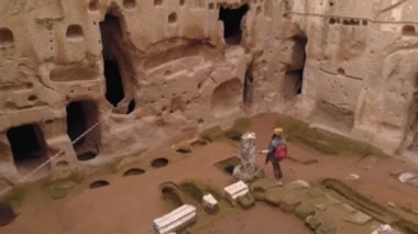 Gumusler mağara manastırında yalnız yürüyen bir kadın. Kapadokya, Türkiye 'de taş duvarlarla çevrili antik mağara manastırında yürüyen bir kız