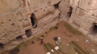 Gumusler mağara manastırında yalnız yürüyen bir kadın. Kapadokya, Türkiye 'de taş duvarlarla çevrili antik mağara manastırında yürüyen bir kız