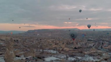 Kapadokya, Türkiye 'de kış mevsiminde karla kaplı perili bacaların üzerinden uçan bir sürü sıcak hava balonunun 4k hava manzarası.