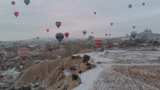 4Kカッパドキア トルコの冬の季節に雪で覆われた妖精の煙突の上を飛ぶ熱気球の多くの空中ビュー — ストック動画