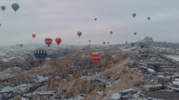 4Kカッパドキア トルコの冬の季節に雪で覆われた妖精の煙突の上を飛ぶ熱気球の多くの空中ビュー — ストック動画