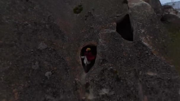 トルコのカッパドキアで雪の冬の風景とパサバグ渓谷の大きな妖精の煙突の中の小さな洞窟の窓に一人で立っている女性の空中叙事詩の景色 — ストック動画