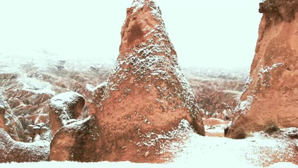 カッパドキアのデバントバレーでの雪景色のシネマティックな空中ビュー 雪に囲まれた妖精の煙突カッパドキアの冬の季節にユニークな凝灰岩の岩の形成でいっぱいの想像上の谷 — ストック動画