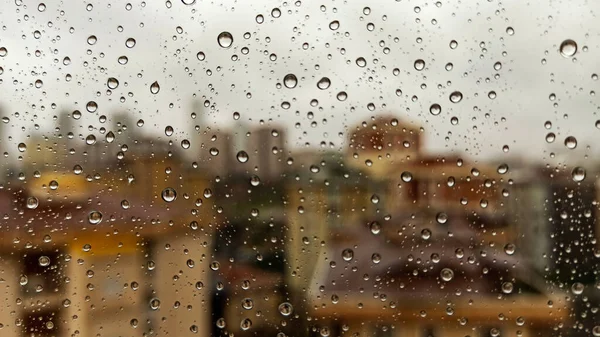 Raindrops on office window with blur grey sky background. Office window covered with closeup rain water.