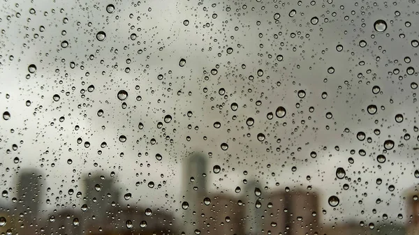 Raindrops on office window with blur grey sky background. Office window covered with closeup rain water.