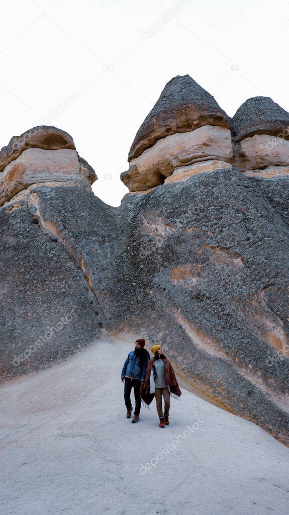 Travel couple walking around rock formations in Pasabag Valley, the valley of the monks in Cappadocia, Happy couple standing near cave houses surrounded by fairy chimneys at Pasabag Valley in Turkey