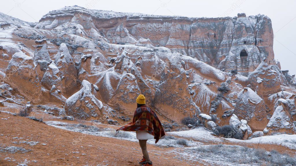 Woman alone with the volcanic landscape at Devrent Valley in Cappadocia. Girl walking around Fairy chimneys surronded by tufa formations at Imaginary Valley in winter season in Cappadocia, Turkey.