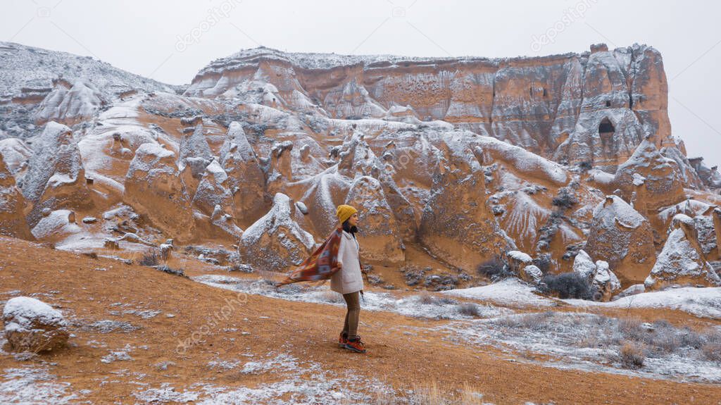 Woman alone with the volcanic landscape at Devrent Valley in Cappadocia. Girl walking around Fairy chimneys surronded by tufa formations at Imaginary Valley in winter season in Cappadocia, Turkey.