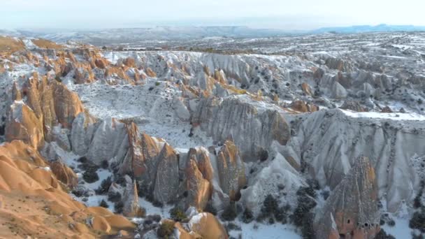 トルコのカッパドキアの日没時に赤谷とローズバレーの空中雪景色 カッパドキアのレッドバレーで雪に覆われたトゥファと岩の形成の空中映画の景色 — ストック動画