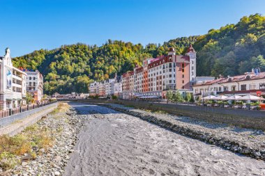 Krasnaya Polyana, Rusya., 10 Ekim 2019: Güneşli bir sonbaharda Mzymta nehri boyunca oteller, dükkanlar ve restoranlar.