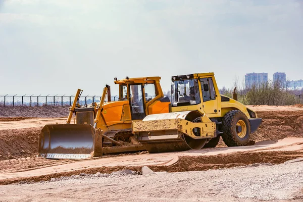 Straßenwalze und Planierraupe stehen beim Straßenneubau auf Sandfläche. — Stockfoto