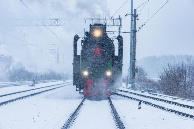 Retro buhar treni kış karlı bir zamanda tren istasyonundan ayrılır..