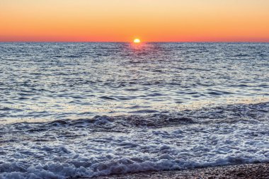 Denizin sakin yüzeyinde gün batımı gökyüzü.