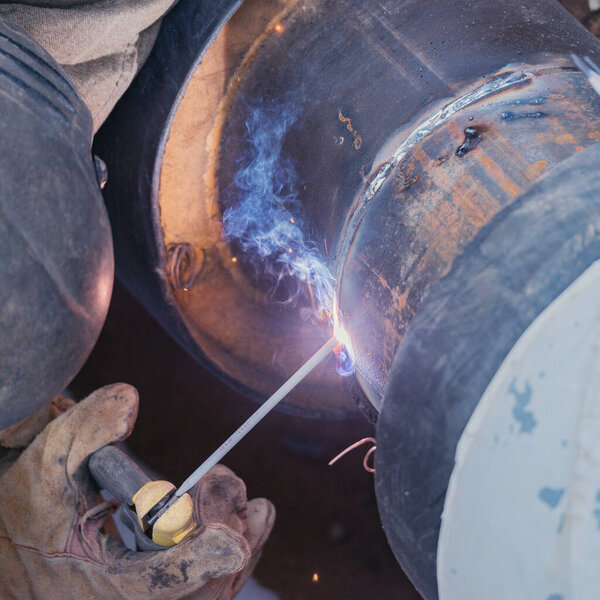 Welder worker welds new metal pipe on the construction site.