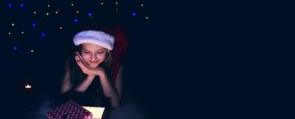暗闇の中に座っている少女は 自宅の寝室にクリスマスギフトボックスを開きます 背景には提灯が見えます — ストック写真