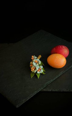 Birkaç tane renkli Paskalya yumurtası. Yakınlarda, karanlık ve lüks bir arka planda çiçek açan bir dal var. Mutlu Paskalyalar. Gastronomik durum.