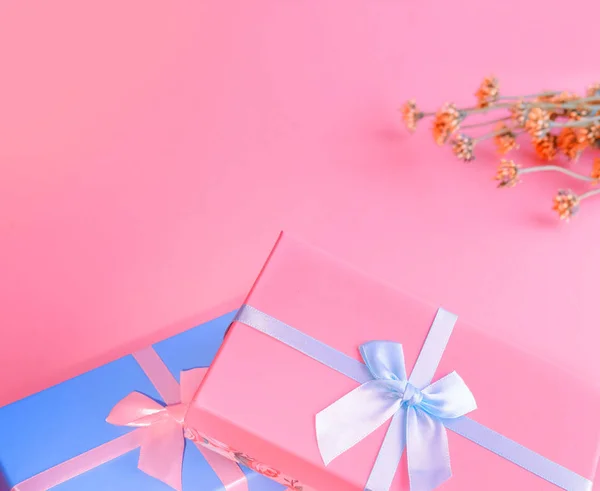 Zwei Schachteln blau und rosa im Vordergrund sind mit Satinbändern gebunden. Wildblumen auf einem trendigen rosa Hintergrund. — Stockfoto