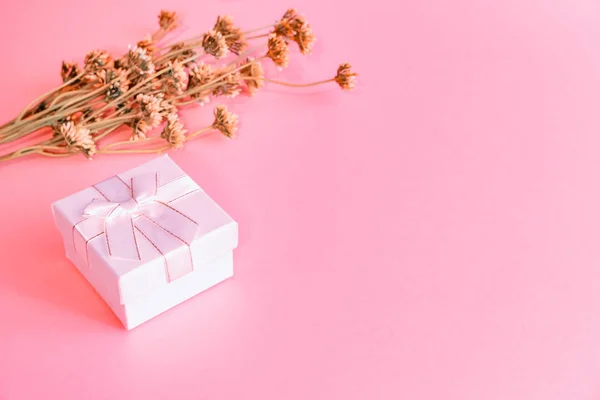 Witte geschenkdoos gebonden met een lint op een roze achtergrond. Tegenover ligt een boeket gele wilde bloemen. Er is een plaats voor tekst.. — Stockfoto