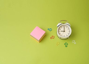 Notlar için yeşil, mavi, pembe, sarı ve ahududu rengirenkli kağıt yaprakları üzerinde beyaz bir arka plan üzerinde bir çalar saat ile Saat