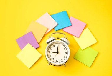 Beyaz alarm saati ve sarı arka planda renkli yapışkan notlar. Çalışma zamanı kavramı. İşyeri