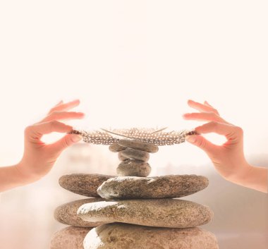Kadının elleri taştan bir piramidin üzerine tüy koydu. Denge, denge konsepti. Zen taşları beyaza
