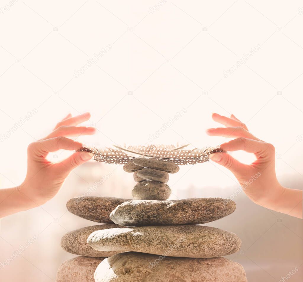 Woman's hands put a feather on a pyramid of stones. Equilibrium, Balance concept. Zen stones on white