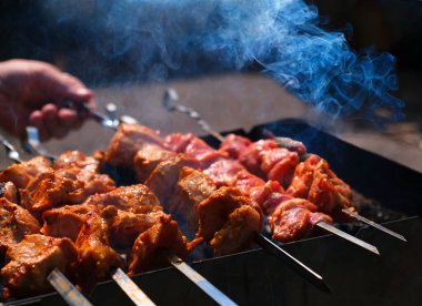 Adam terbiye edilmiş şiş kebap pişiriyor, kuzu eti metal şişte ızgara yapıyor, mavi duman, yakın çekim. Odaklanmamış