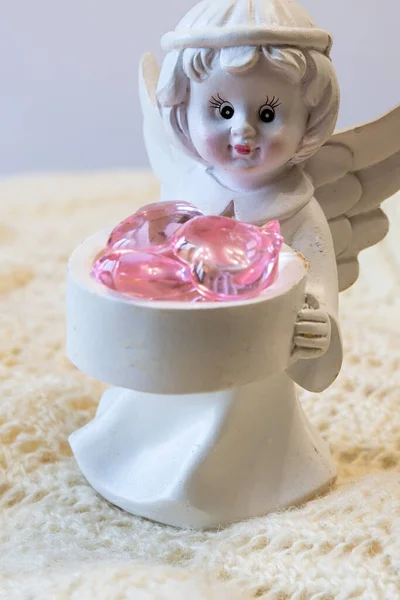 Biała ceramiczna figurka anioła trzymającego kosz z różowymi sercami, na jasnym tle — Zdjęcie stockowe