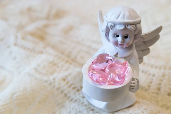 Figura de cerámica blanca de un ángel sosteniendo una cesta con corazones rosados, sobre un fondo claro —  Fotos de Stock