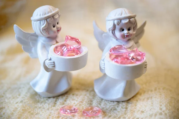 Figurine en céramique blanche d'un ange tenant un panier avec des cœurs roses, sur un fond clair — Photo