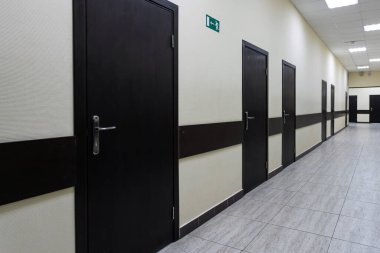 Modern ofis binasının boş koridoru. Bej duvarlı çok uzun bir koridor boyunca bir sürü kahverengi kapı var..