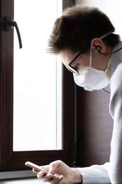 Yeniden kullanılabilir tıbbi maskeli genç bir adam kendini koronavirüsten nasıl koruyacağına dair bilgi almak için telefon ekranına bakar.