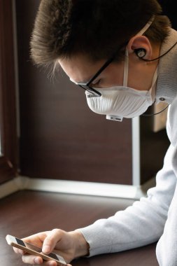 Yeniden kullanılabilir tıbbi maskeli genç bir adam kendini koronavirüsten nasıl koruyacağına dair bilgi almak için telefon ekranına bakar.