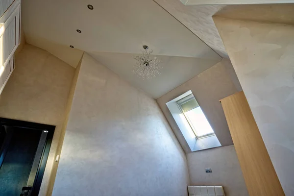 Light multistage plastered ceiling in a modern attic room with a Dormer window