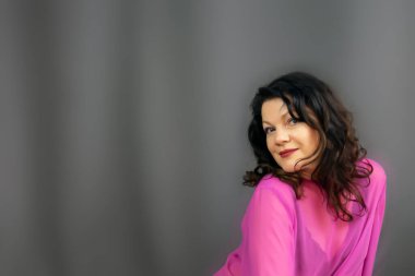 Parlak, yarı şeffaf, yarı şeffaf elbisesi olan, koyu gri bir arka planda poz veren orta yaşlı güzel bir kadının portresi. Her yaşta gençliği koruma kavramı.