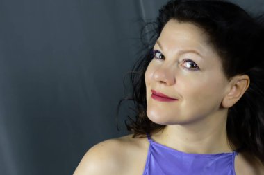 Koyu gri bir arka planda poz veren, uzun siyah saçlı, orta yaşlı güzel bir kadının portresi. Her yaşta gençliği koruma kavramı.