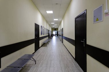 Modern ofis binasının boş koridoru. Bej duvarlı çok uzun bir koridor boyunca bir sürü kahverengi kapı var..