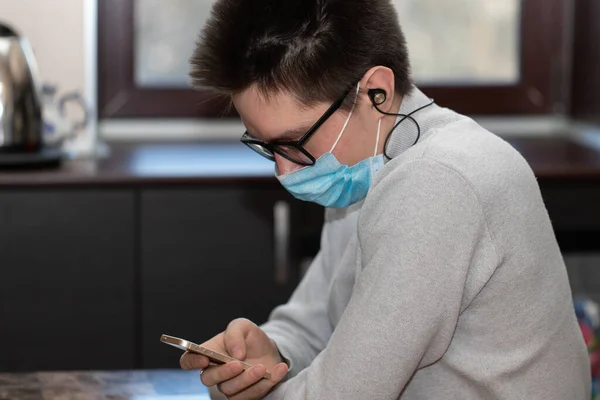Yeniden kullanılabilir tıbbi maskeli genç bir adam telefon ekranına bakar ve arkadaşlarının mesajlarını okur. Bir salgın sırasında iletişim.