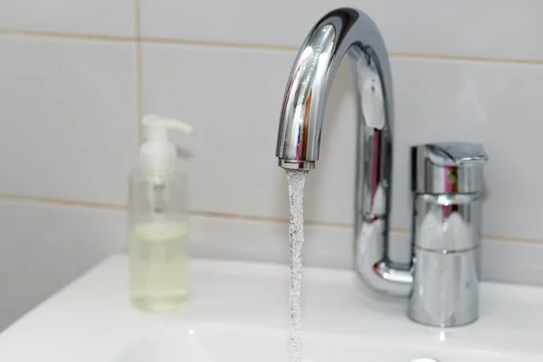 Modern hand wash basin. Solid tabletop surface and gray tile wall. Dispensable soap next to water tap on bathroom sink