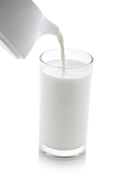 Milch aus einem Krug in ein Glas auf weißem Hintergrund gießen — Stockfoto