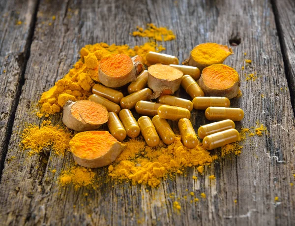 Turmeric powder and turmeric capsules on wooden background