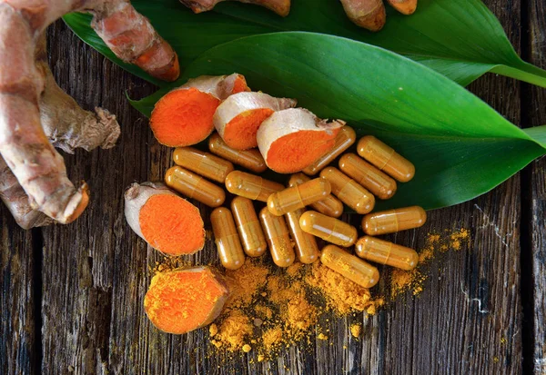 Turmeric powder and turmeric capsules on wooden background